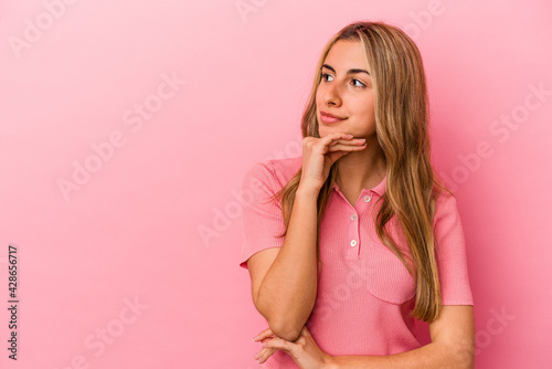 Young blonde caucasian woman isolated on pink background looking sideways with doubtful and skeptical expression.