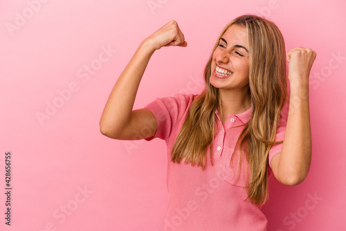 Young blonde caucasian woman isolated on pink background raising fist after a victory, winner concept.