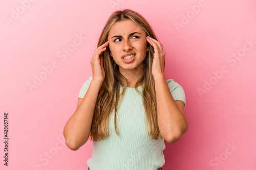 Young blonde caucasian woman isolated on pink background covering ears with fingers, stressed and desperate by a loudly ambient.