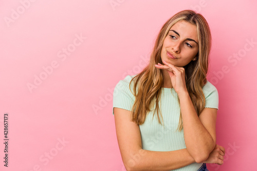 Young blonde caucasian woman isolated on pink background looking sideways with doubtful and skeptical expression.