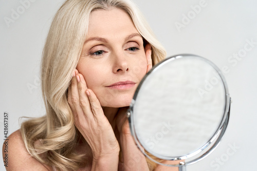Closeup portrait of gorgeous happy middle age woman looking at mirror touching her skin enjoying treatment for dry skin. Advertising of antiaging beauty skin care products. photo