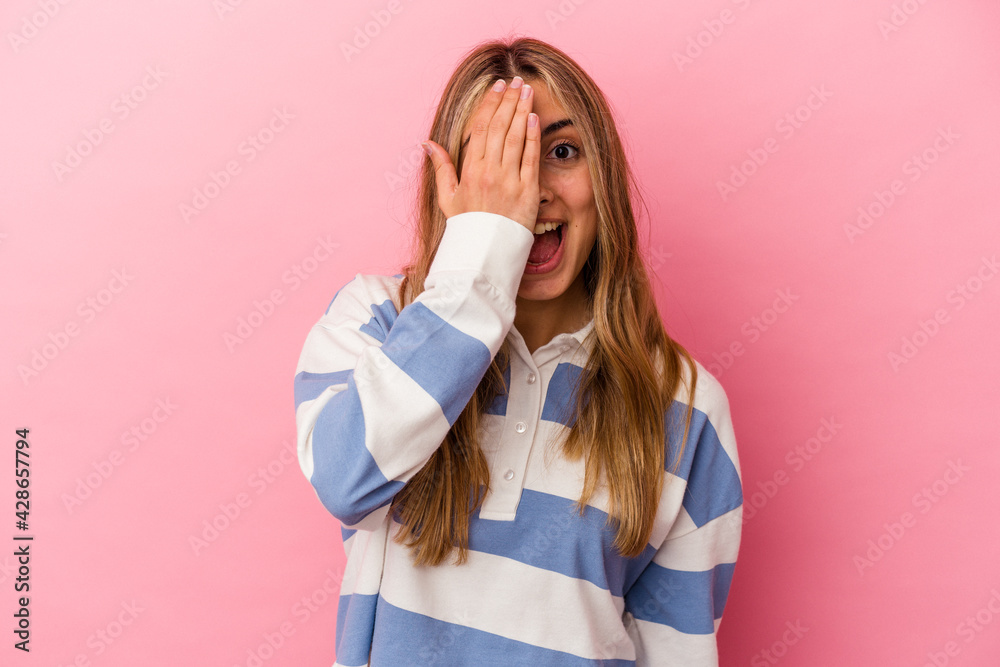 Young blonde caucasian woman isolated on pink background having fun covering half of face with palm. Young blonde caucasian woman isolated on pink background having fun covering half of face with palm.