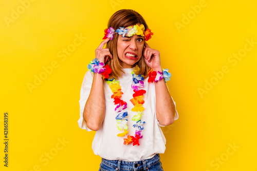 Young caucasian woman celebrating a hawaiian party isolated on yellow background covering ears with hands.