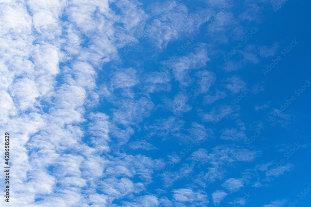 Blue sky background with textured white clouds on a clear day.