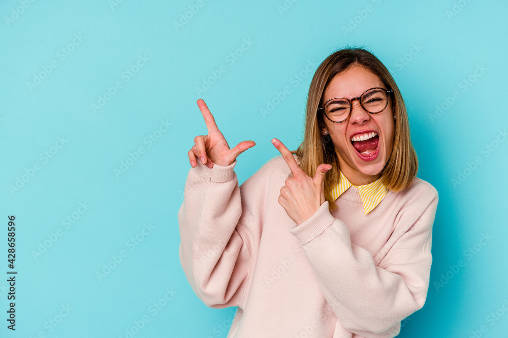 Young student caucasian woman isolated on blue background pointing with forefingers to a copy space, expressing excitement and desire.