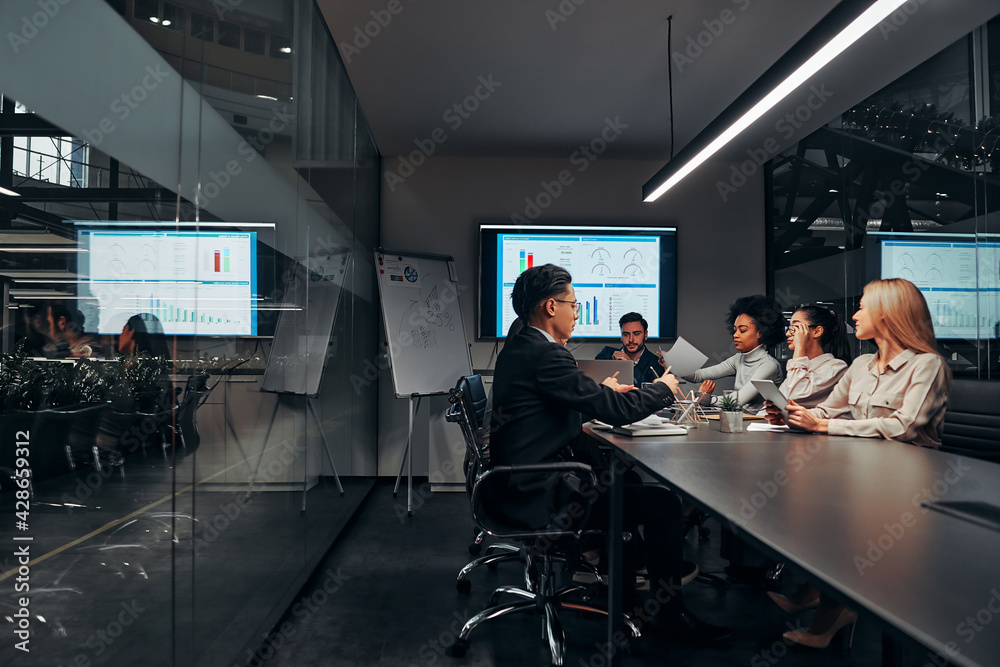 Work team. A group of successful business people work hard in the conference room of a large spacious office. In the room there is a monitor with graphs and a flipchart with a plan. Work team. A group of successful business people work hard in the conference room of a large spacious office. In the room there is a monitor with graphs and a flipchart with a plan.