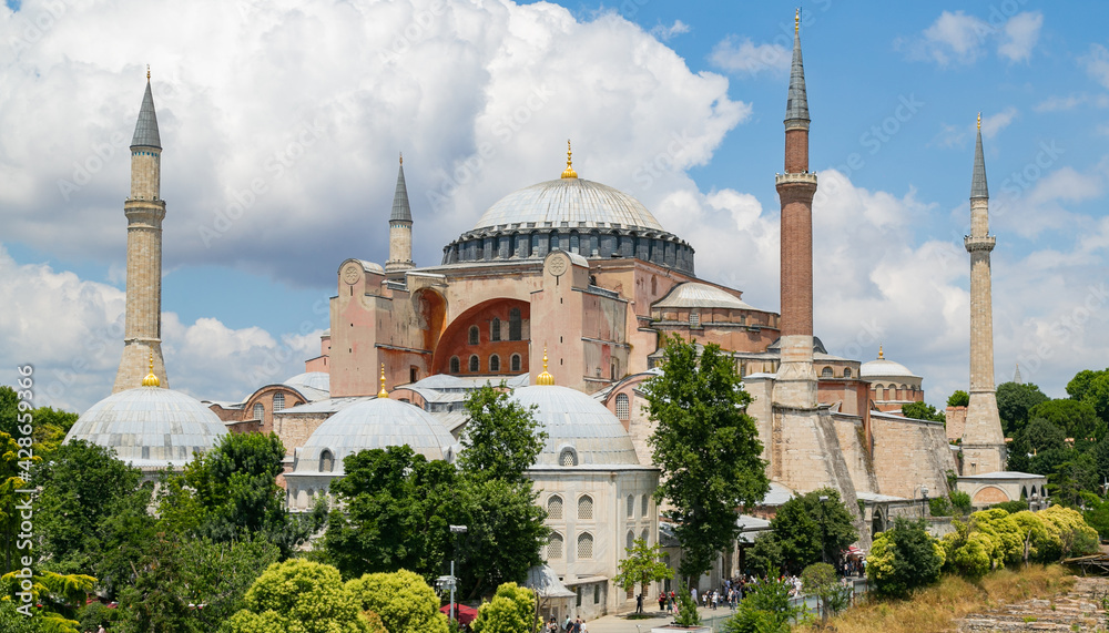 Obraz premium Hagia Sophia in summer, Istanbul, Turkey. The world famous monument of Byzantine architecture, imperial mosque and now a museum. View of the St. Sophia Cathedral with cloudy sky and green trees.