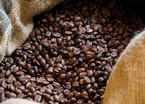 Selective focus on jute bag full of fresh roasted arabian coffee beans, closeup photo can be used as background of commercial ad with copy space area