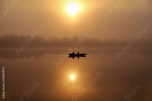 Morning. river  silhouette of a boat and fishermen  beautiful sunlight  reflection in the water of trees and the sun  a married couple in a boat  morning fishing  trolling  blur
