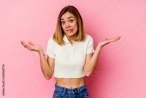 Young caucasian woman isolated on pink background confused and doubtful shrugging shoulders to hold a copy space.