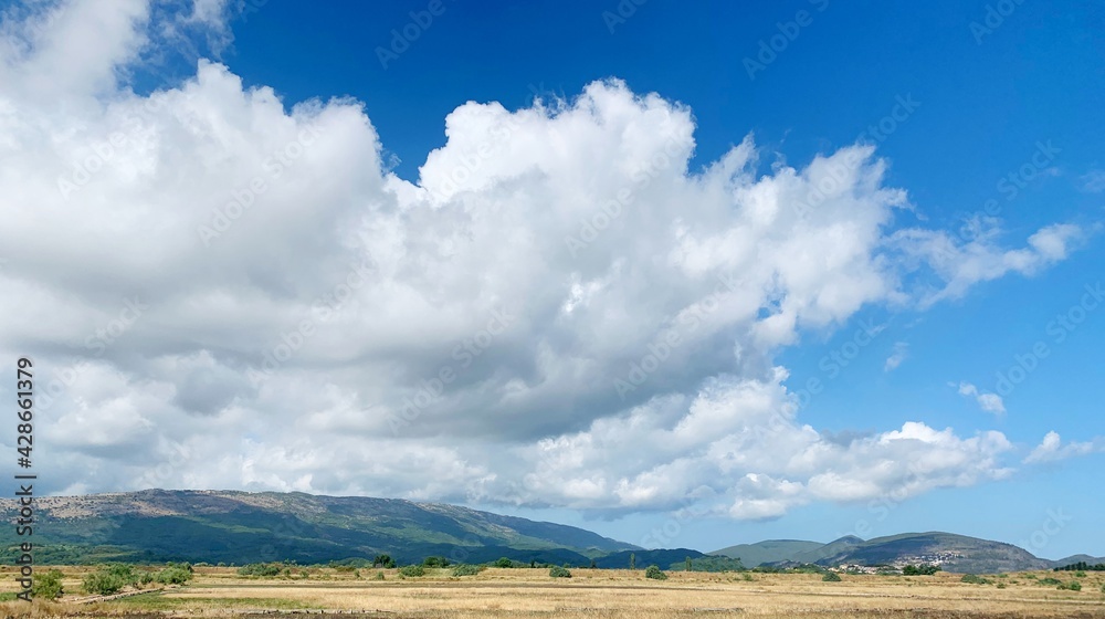 Sky clouds landscape.  Impressive cloudscape over summer fields and mountain. Huge cloud in heaven. Sunlight.