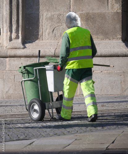 Varredor de rua com carrinho e uniforme de cores fluorescentes e refletoras - trabalho, profissão de limpeza de cidades photo