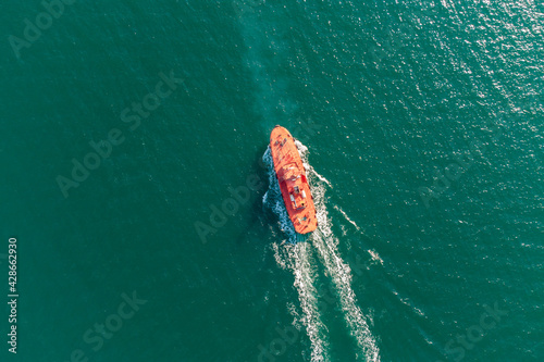 The pilot boat orange goes to meet the vessel on the outer roads. Helicopter view. Top view of the sea.