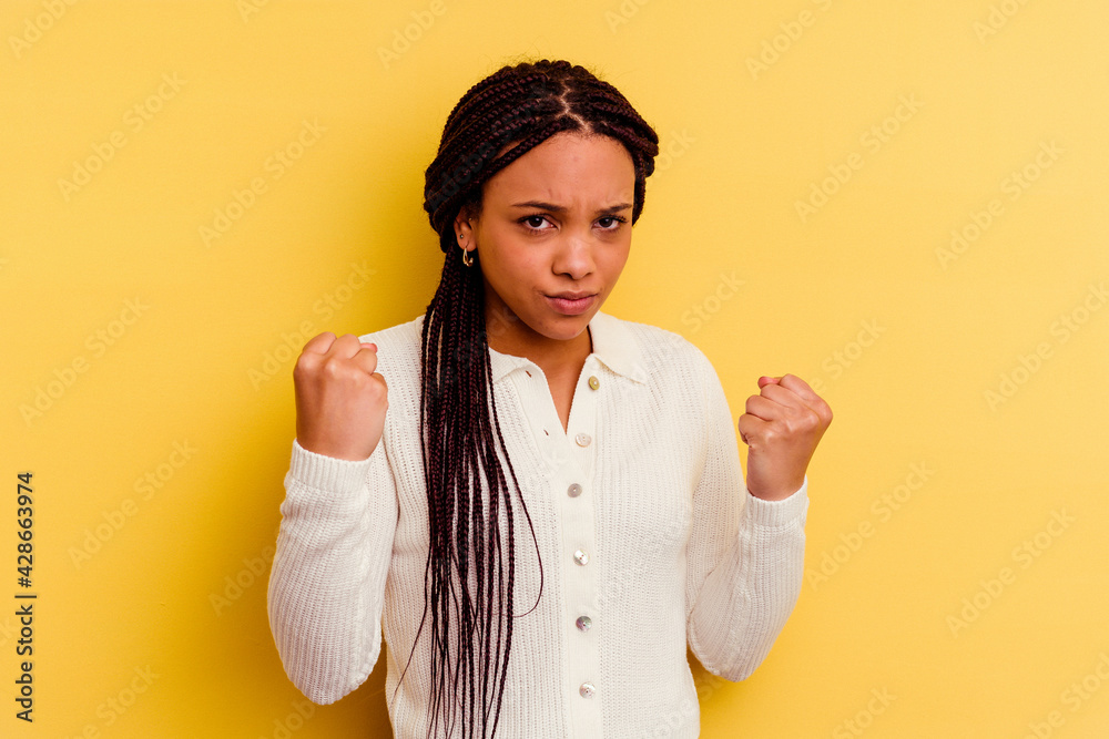 Young african american woman isolated on yellow background showing fist to camera, aggressive facial expression. Young african american woman isolated on yellow background showing fist to camera, aggressive facial expression.