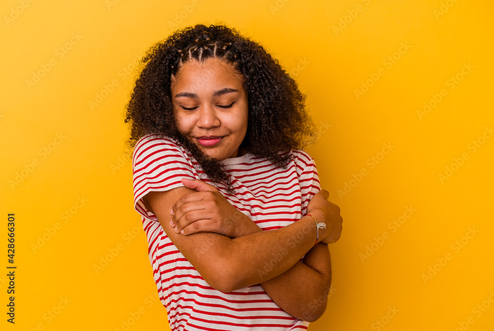 Young african american woman isolated on yellow background hugs, smiling carefree and happy. Young african american woman isolated on yellow background hugs, smiling carefree and happy.
