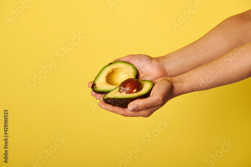 Closeup of hands holding two halves of ripe ready-to-eat avocado
