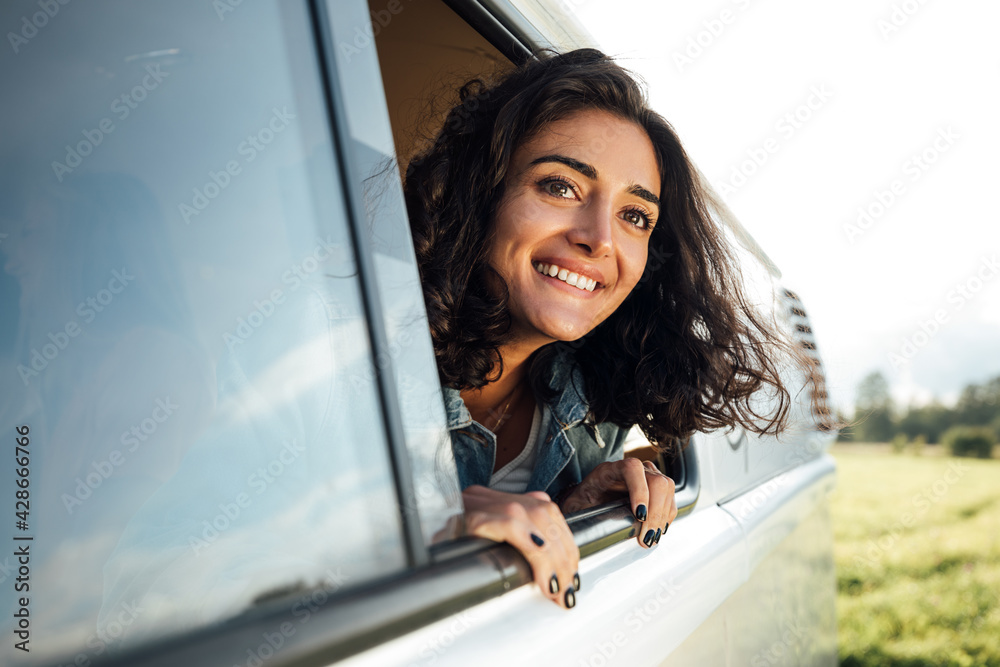 Beautiful brunette looks out of a window enjoying a road trip. Young woman in camper van looking into a distance.