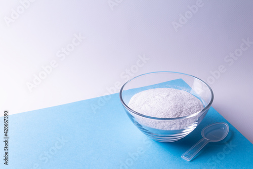 Glass plate with collagen powder and measuring spoon on a blue background.