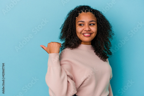 Young african american woman isolated on blue background points with thumb finger away, laughing and carefree.