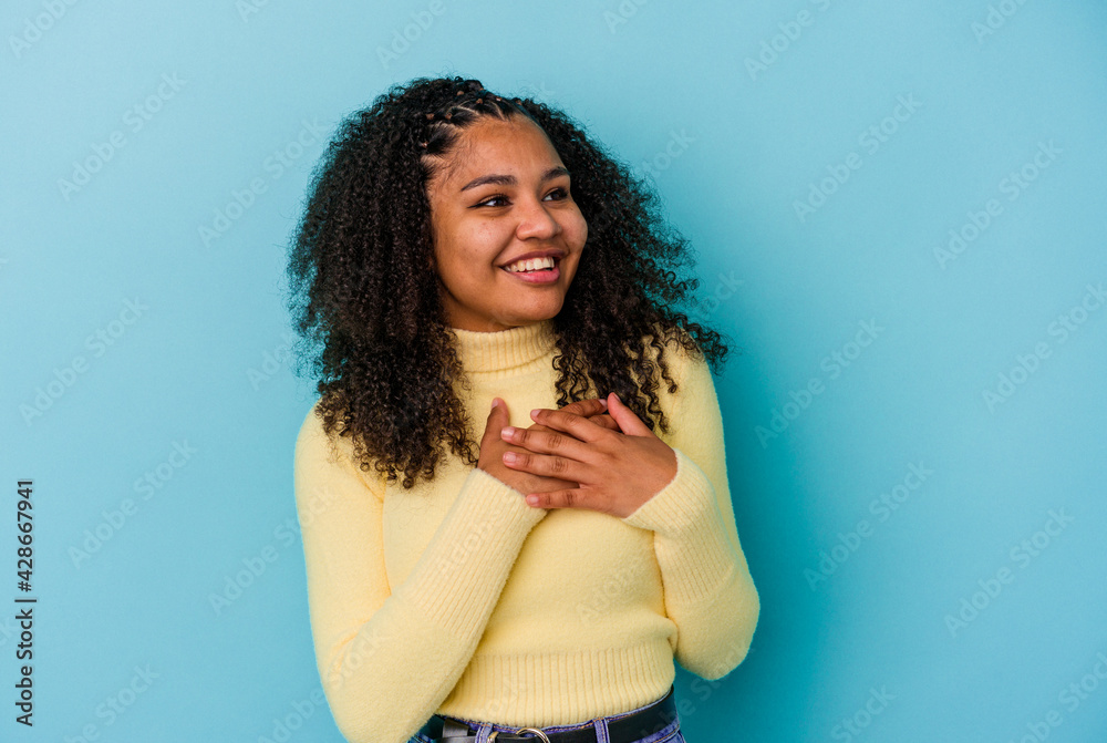Young african american woman isolated on blue background laughing keeping hands on heart, concept of happiness. Young african american woman isolated on blue background laughing keeping hands on heart, concept of happiness.