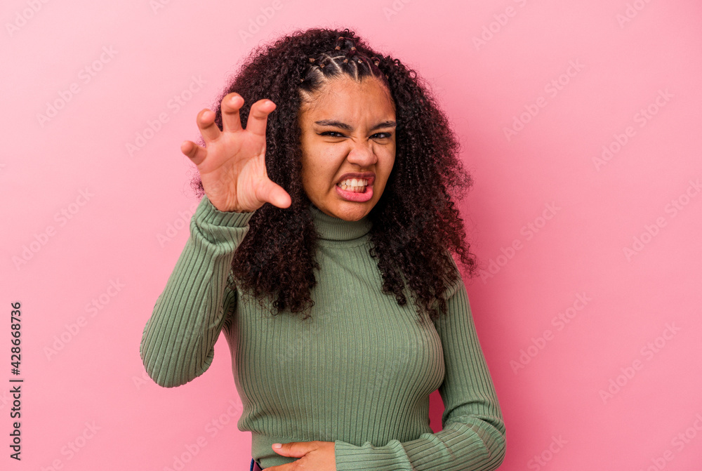 Young african american woman isolated on pink background showing claws imitating a cat, aggressive gesture. Young african american woman isolated on pink background showing claws imitating a cat, aggressive gesture.