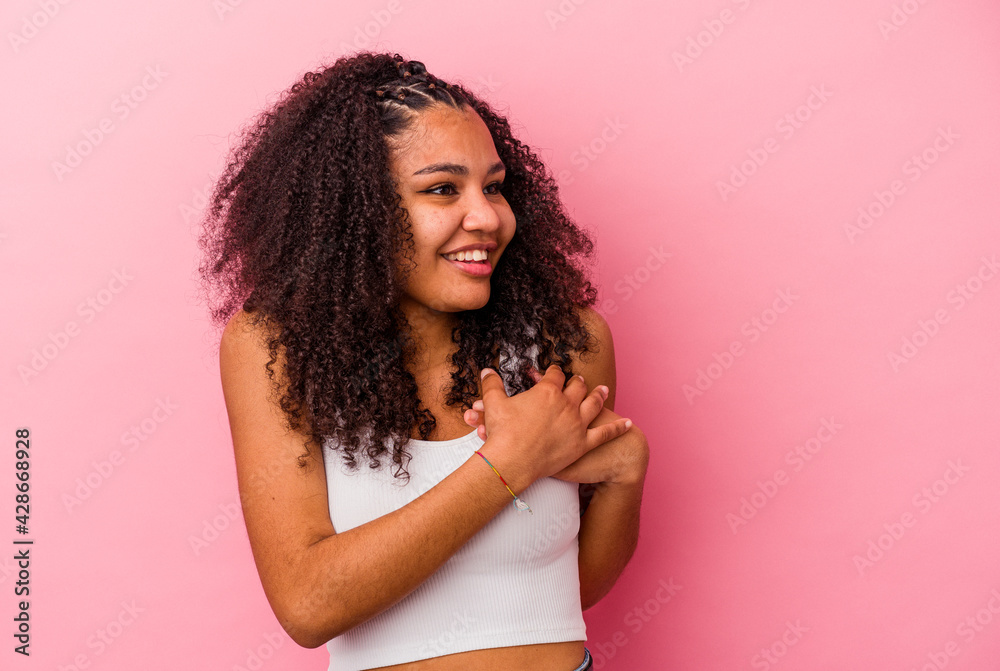 Young african american woman isolated on pink background laughing keeping hands on heart, concept of happiness. Young african american woman isolated on pink background laughing keeping hands on heart, concept of happiness.