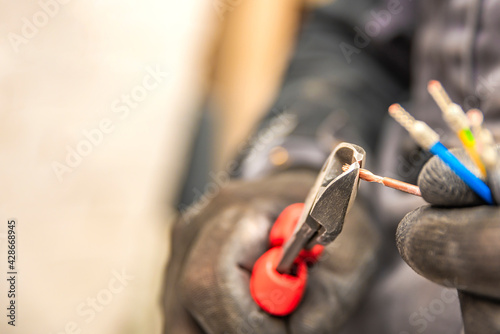 Electrician hands hold wire cutters and close-up of wires. The idea of repairing and connecting electrical wiring at home or at work