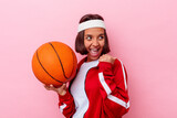 Young mixed race woman playing basketball isolated on pink background points with thumb finger away, laughing and carefree.
