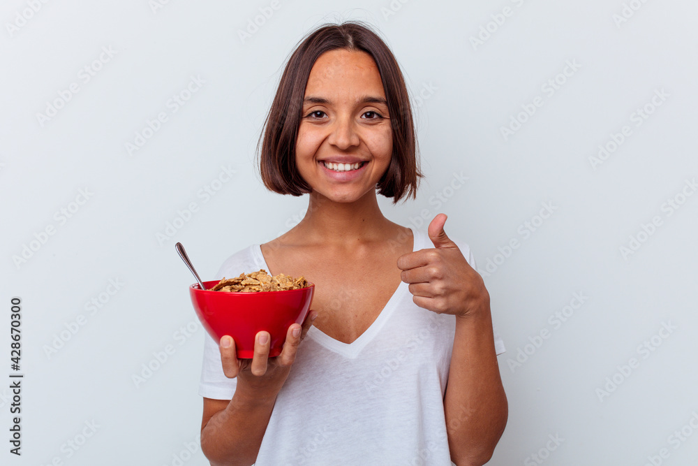 Young mixed race woman eating cereals isolated on white background smiling and raising thumb up Young mixed race woman eating cereals isolated on white background smiling and raising thumb up
