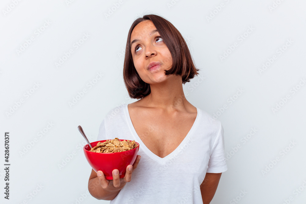 Young mixed race woman eating cereals isolated on white background dreaming of achieving goals and purposes