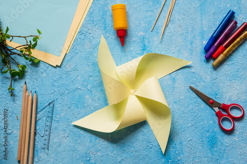 Step-by-step making of a paper weather vane by a child on a blue concrete background. Children's creativity, divas, crafts.