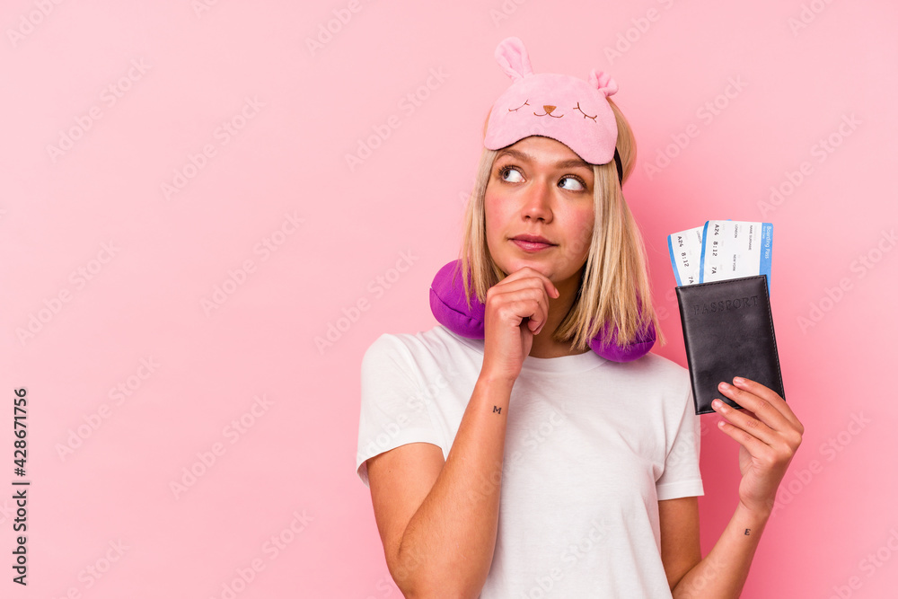 Young venezuelan traveler woman holding a passport isolated on pink background looking sideways with doubtful and skeptical expression. Young venezuelan traveler woman holding a passport isolated on pink background looking sideways with doubtful and skeptical expression.