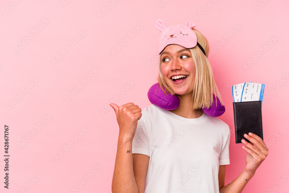 Young venezuelan traveler woman holding a passport isolated on pink background points with thumb finger away, laughing and carefree. Young venezuelan traveler woman holding a passport isolated on pink background points with thumb finger away, laughing and carefree.