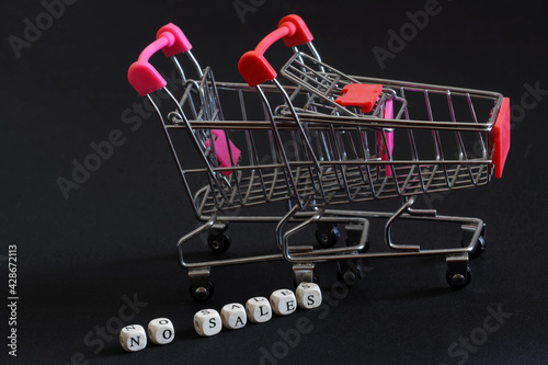 Two empty metal carts from the supermarket and the inscription no sales on a black background. The concept of economic crisis, scarcity and lack of purchases. Free space for an inscription