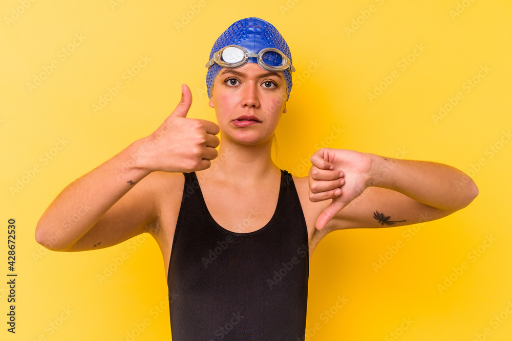 Young swimmer venezuelan woman isolated on yellow background showing thumbs up and thumbs down, difficult choose concept Young swimmer venezuelan woman isolated on yellow background showing thumbs up and thumbs down, difficult choose concept