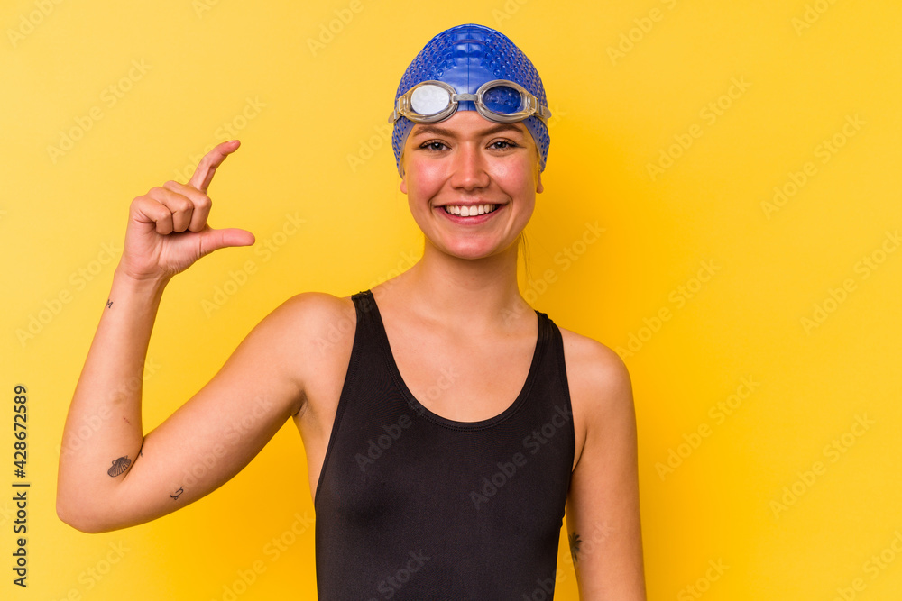 Young swimmer venezuelan woman isolated on yellow background holding something little with forefingers, smiling and confident. Young swimmer venezuelan woman isolated on yellow background holding something little with forefingers, smiling and confident.