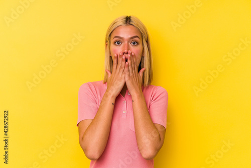Young venezuelan woman isolated on yellow background shocked, covering mouth with hands, anxious to discover something new.