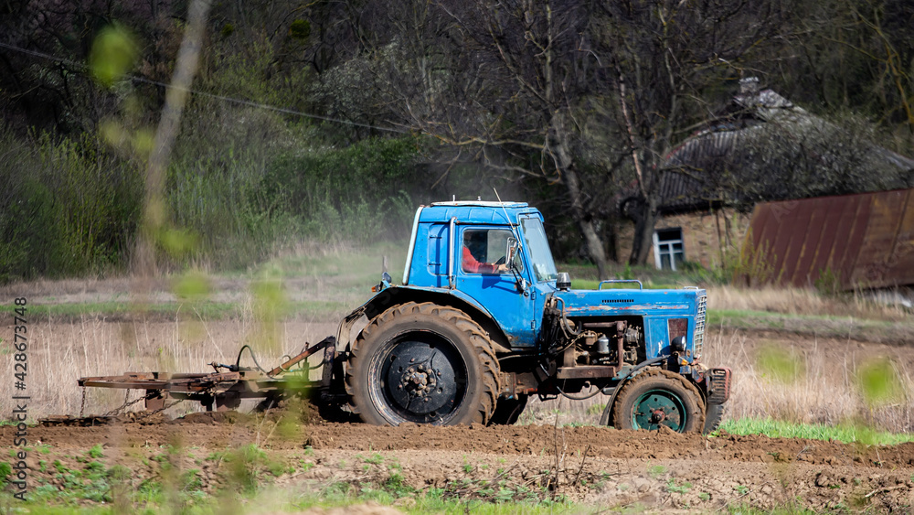 old blue tractor with plow on field and cultivates soil. Preparing the soil for planting vegetables in spring. Agricultural machinery, field work. old blue tractor with plow on field and cultivates soil. Preparing the soil for planting vegetables in spring. Agricultural machinery, field work.