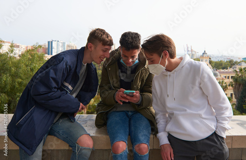 A closeup of three young Caucasian and Hispanic guys sitting and looking at one smartphone
