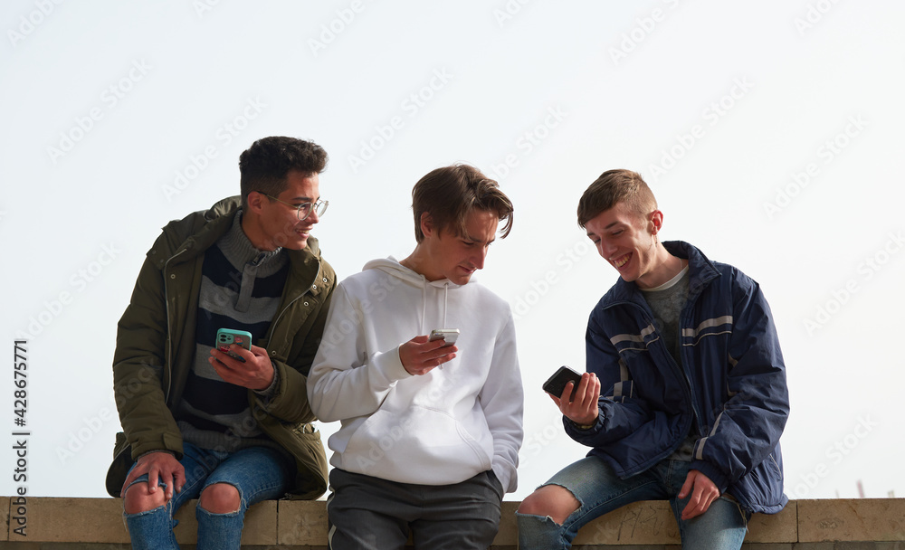 A closeup of three young Caucasian and Hispanic guys socializing and using their smartphones A closeup of three young Caucasian and Hispanic guys socializing and using their smartphones