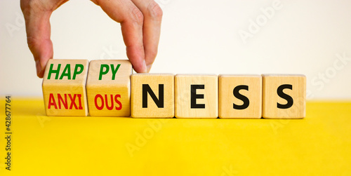Happyness or anxiousness. Doctor turns cubes and changes the word 'anxiousness' to 'happyness'. Beautiful yellow table, white background. Psychological, happyness or anxiousness concept. Copy space. photo