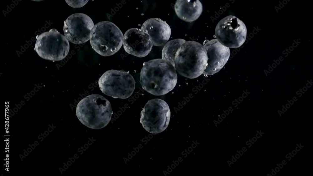 Fresh juicy blueberries fall into the water with bubbles in slow motion. Fruits on isolated black background. Fresh juicy blueberries fall into the water with bubbles in slow motion. Fruits on isolated black background.