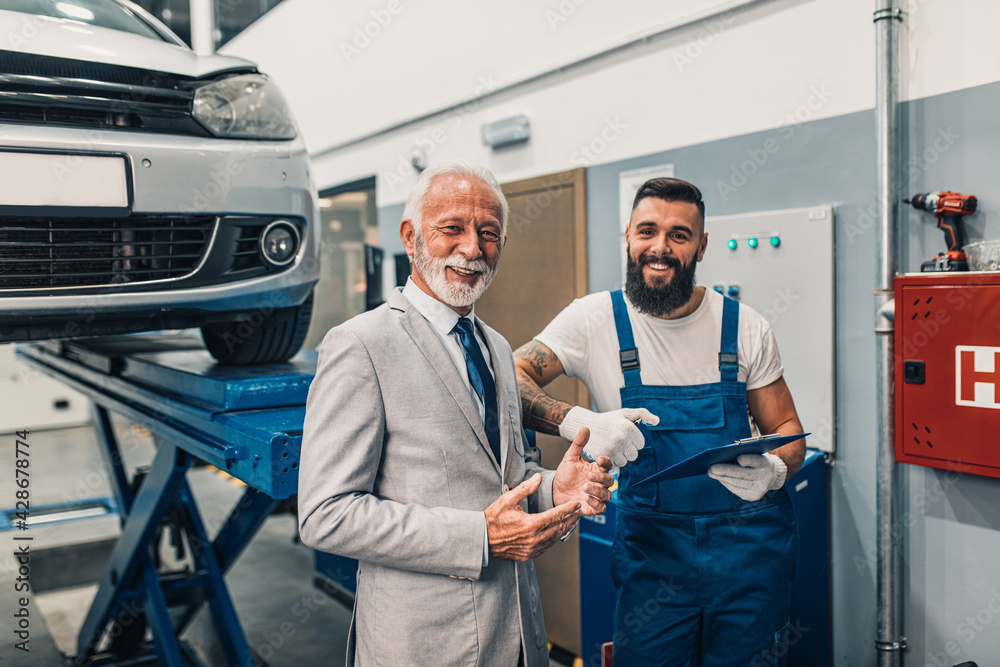 Fototapeta premium Car mechanic talking with senior business man costumer during periodic car condition check. Technical inspection.