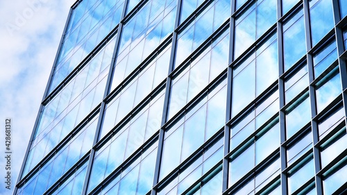 Abstract closeup of the glass-clad facade of a modern building covered in reflective plate glass. Architecture abstract background. Glass wall and facade detail. Velvia graphic filter.