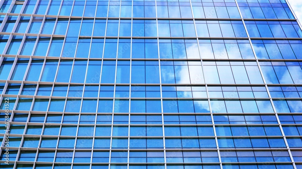 Abstract closeup of the glass-clad facade of a modern building covered in reflective plate glass. Architecture abstract background. Glass wall and facade detail. Velvia graphic filter.