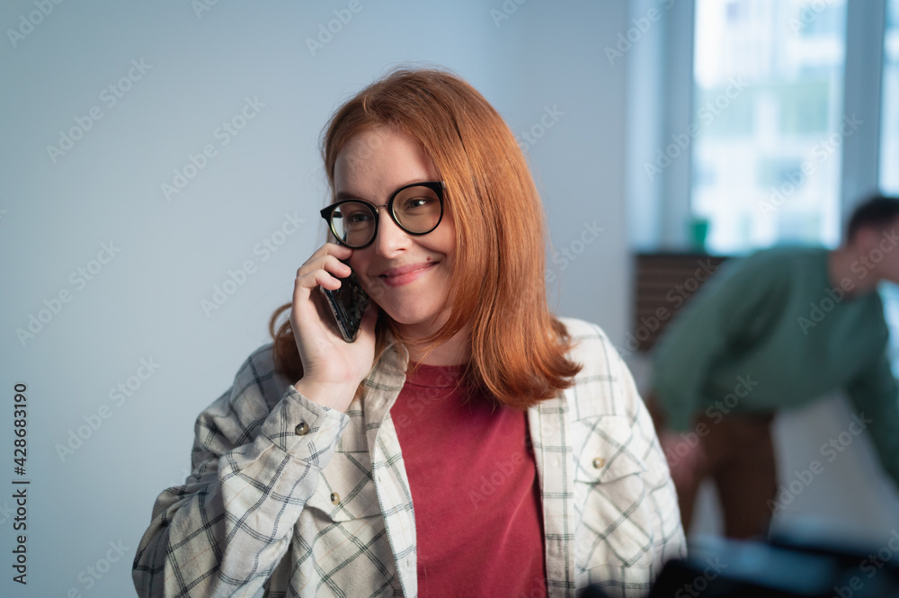 Portrait of a young girl with glasses, talking on the phone in her new apartment against the background of windows and walls Portrait of a young girl with glasses, talking on the phone in her new apartment against the background of windows and walls