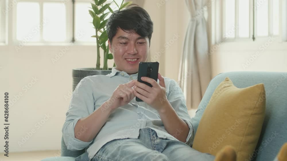 Male Lying On Sofa And Using Smartphone In Living Room