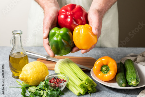 Fototapeta Naklejka Na Ścianę i Meble -  Healthy food fresh local vegetables red, green and yellow peppers, zucchini and celery in the hands of the chef. Vegetables for fresh salad with olive oil and lemon. Mediterranean diet vegan food