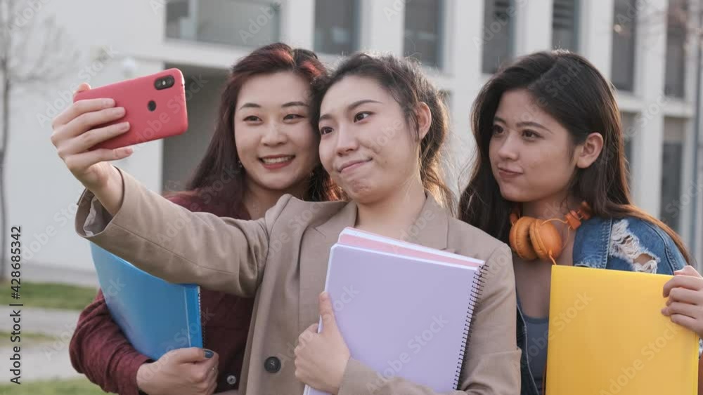 Asian college students taking a selfie with a mobile phone while standing outside the university campus. Education concept. Asian college students taking a selfie with a mobile phone while standing outside the university campus. Education concept.