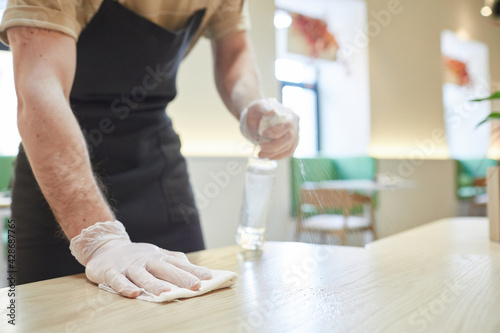 Close up of unrecognizable man sanitizing tables and cleaning furniture in cafe, copy space